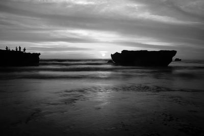 Silhouette rocks on beach against sky during sunset