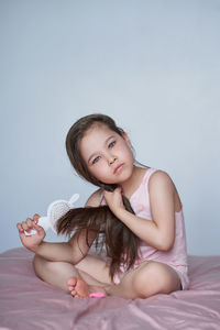 The girl is sitting on the bed and combing her long hair.