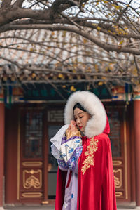 Woman wearing traditional clothing praying while standing outside temple