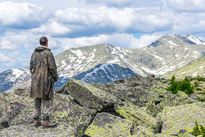 A man stands on a rock and looks towards the mountain peaks