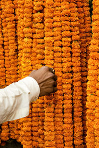 Cropped image of hand touching marigold garlands at market