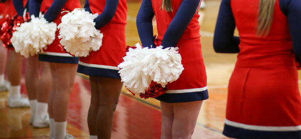 Cheerleader's with their pom poms behind their backs while watching their basketball team.