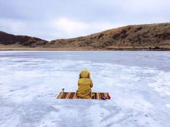 Rear view of a person sitting on frozen lake