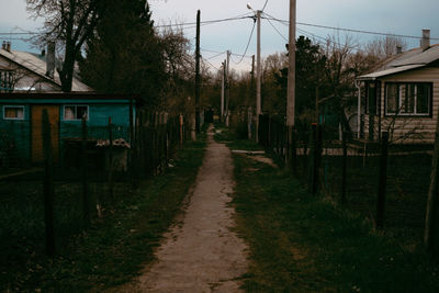 Footpath amidst trees and houses against sky