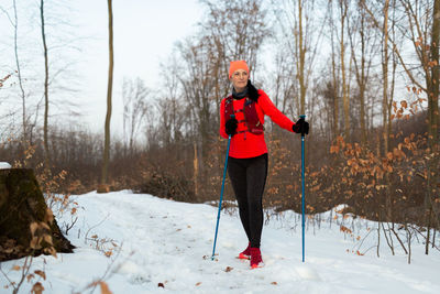 Female runner with trekking poles resting in forest after nordic running in winter.