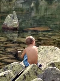 Rear view of shirtless boy standing on rock