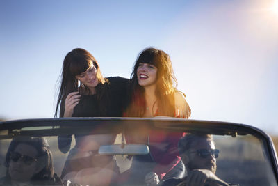 Friends traveling in convertible against clear sky