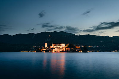 Illuminated buildings by sea against sky at dusk