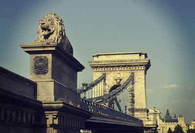 Low angle view of lion statue at chain bridge against sky