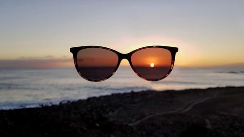 Close-up of sunglasses against sky during sunset