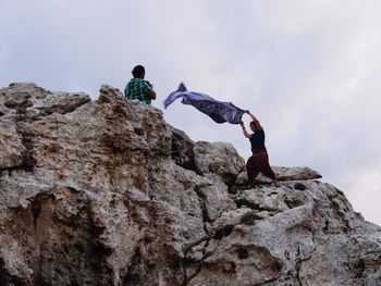 Low angle view of men on rock against sky