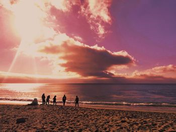 Silhouette people on beach against sky during sunset