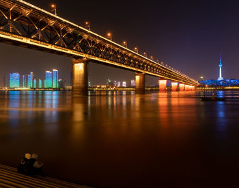 Illuminated bridge over river at night