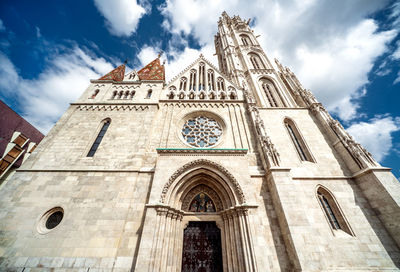 Low angle view of matthias church against cloudy sky during sunny day