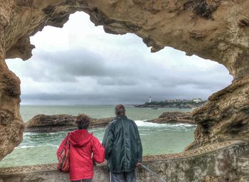 Rear view of people looking at sea against cloudy sky