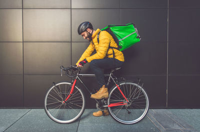 Side view of man sitting on bicycle against wall