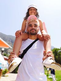Low angle view of father carrying daughter on shoulders against sky