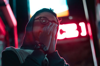 Portrait of young man covering mouth against illuminated sign board