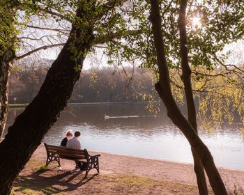 Rear view of man sitting on bench by lake