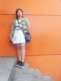 Young woman standing on steps against orange wall