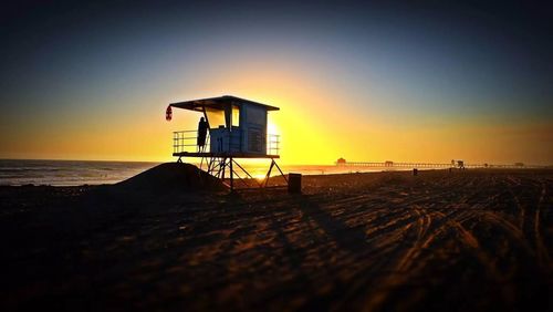 Lifeguard hut on beach against clear sky at sunset