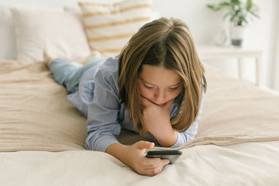 Young woman using phone while lying on bed at home