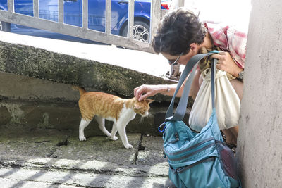 High angle view of woman petting stray cat on footpath
