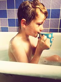 Side view of shirtless boy drinking coffee in bathtub