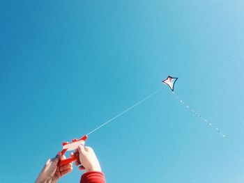 Close-up of hands flying kite against clear blue sky
