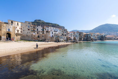 People on beach by buildings against sky in city