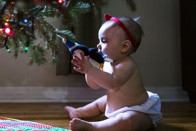 Naughty cute girl baby with red ribbon in her hair pulling christmas ornament from tree