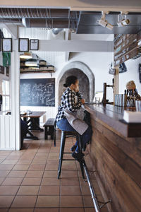 Side view of female bartender using laptop while sitting at bar counter