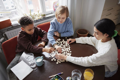 Girl and boys playing scrabble at dining table