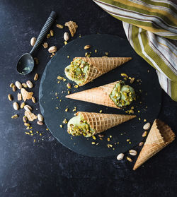 Overhead view of pistachio ice cream in cones on black background.