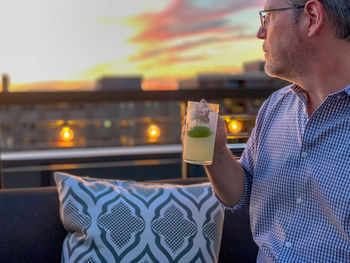 Mature man having drink against sky during sunset