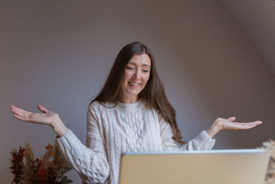 Portrait of young woman talking via laptop showing insecurity with her hands