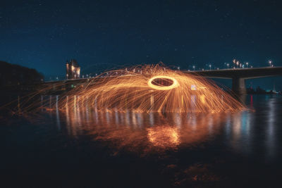 Illuminated bridge over river against sky at night