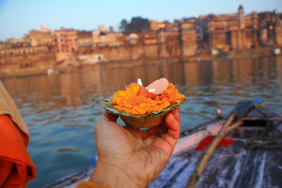 Cropped image of hand holding ice cream against river and buildings