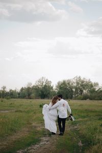 Newlywed couple walking on field against sky