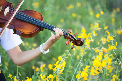 Woman playing violin by yellow flowers on field