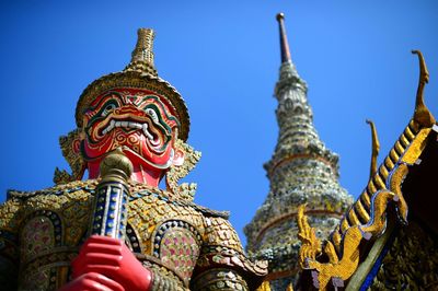 Low angle view of statue by wat phra kaew against clear blue sky