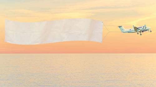 Airplane flying over sea against orange sky