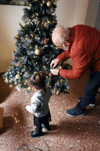 Grandparents decorate the christmas tree with their little granddaughter