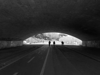 Silhouette people walking on road in tunnel