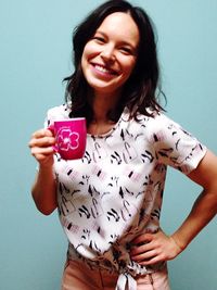 Portrait of smiling young woman drinking against white background