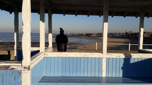 Rear view of man standing on railing at beach
