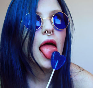 Young woman wearing blue sunglasses licking heart shape candy