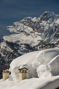 Snow covered house by mountain against clear blue sky