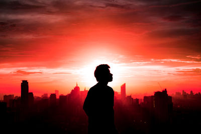 Silhouette man standing by buildings against sky during sunset