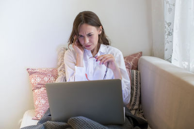 Woman with headache using laptop while sitting at home